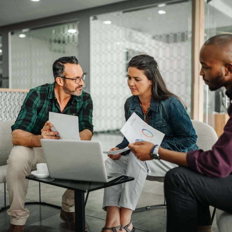 three team members meet in front of a computer with documents with graphs